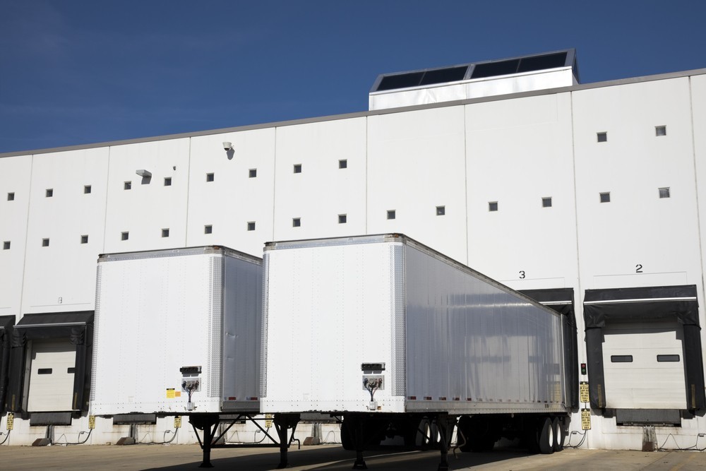 Two trailers parked outside of a warehouse